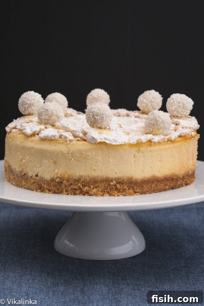 Raffaello Cheesecake on a cake stand, showcasing its elegant white appearance and festive garnishes.