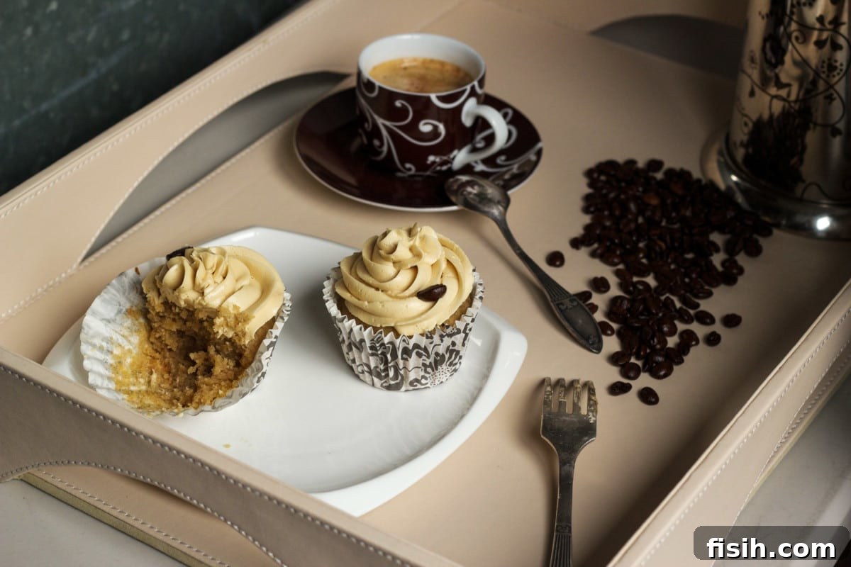 Two exquisitely frosted pumpkin spice latte cupcakes elegantly arranged on a pristine white plate, accompanied by a small espresso cup and a scattering of aromatic coffee beans, visually reinforcing the coffee theme.