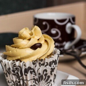 Close-up of a perfectly frosted pumpkin spice latte cupcake with a steaming cup of coffee in the background, showcasing its rich texture and appealing decoration.