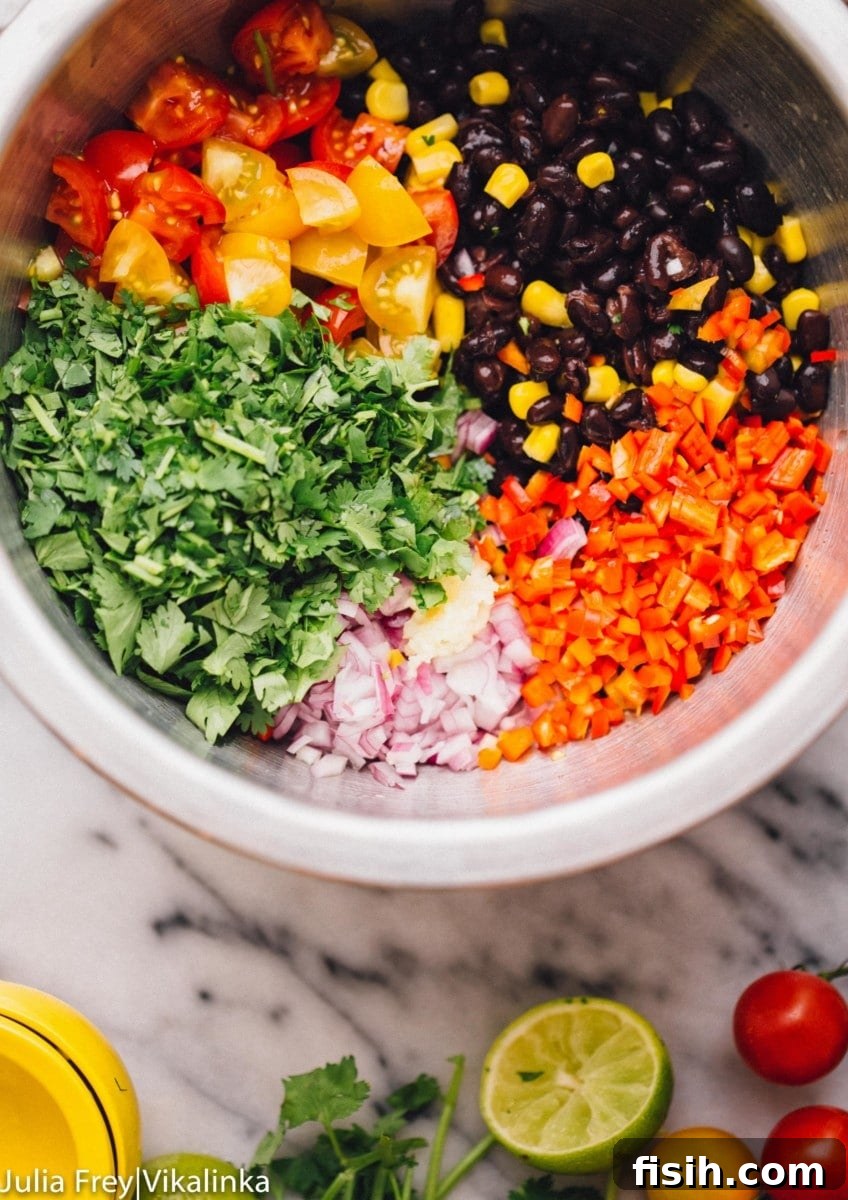 A close-up shot of all the fresh, colorful ingredients for Black Bean and Corn Salsa, including cherry tomatoes, red onion, and fresh lime, gathered in a gleaming metal bowl.