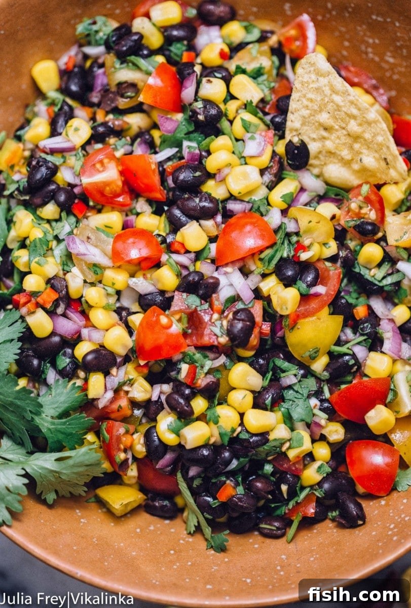 Close-up of freshly prepared Black Bean and Corn Pico de Gallo, garnished with fresh cilantro, served in a rustic brown bowl, emphasizing its vibrant textures and colors.