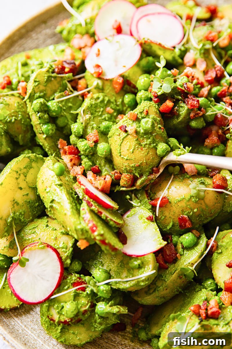 Close-up of Pesto Potato Salad featuring perfectly cooked potato chunks, vibrant sliced radishes, bright green peas, and savory crispy bacon pieces.