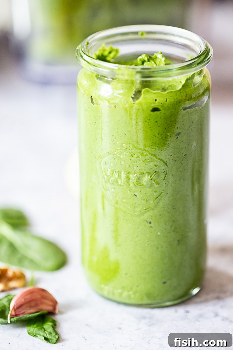 Freshly made spinach pesto presented in a clear mason jar, highlighting its vibrant green color and inviting texture.