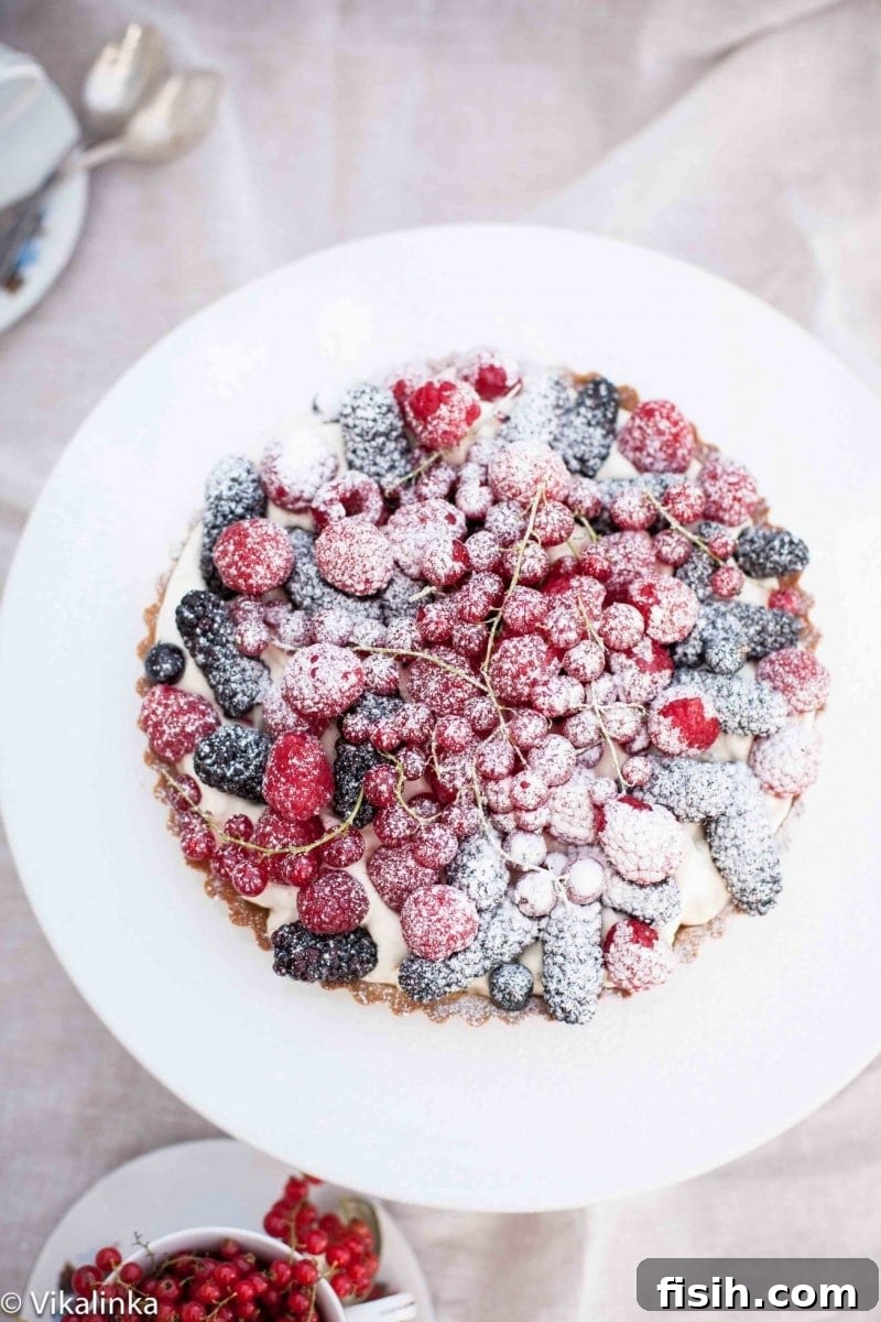 Top down of summer Berry Tart on white platter, showcasing vibrant mixed berries and a delicate crust.