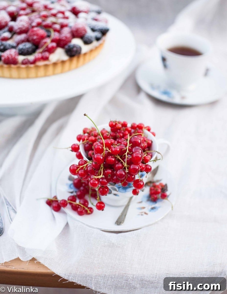 Close up of vibrant cranberries in a bowl with a tea cup and baked tart in the background, highlighting freshness.