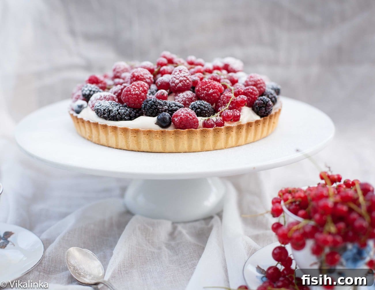 Shot of the impressive Summer Berry Tart displayed on a cake stand, with more cranberries artfully arranged in the foreground.