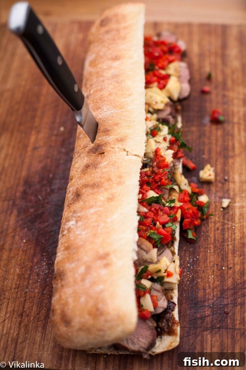 Top down view showing a ciabatta loaf generously topped with sliced duck breast, roasted red peppers, artichokes, and fresh parsley.