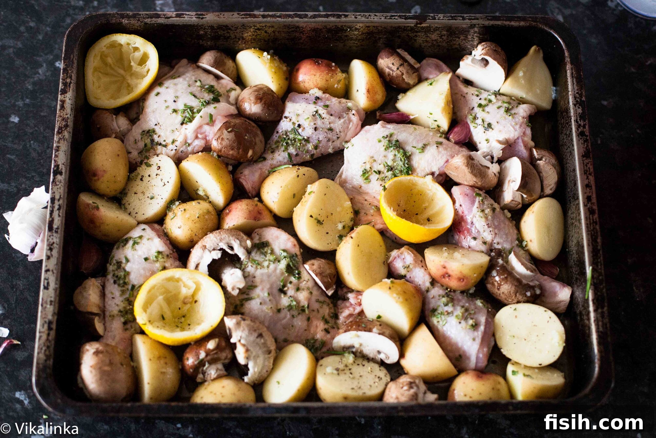A close-up shot of raw chicken thighs and potatoes coated in a fragrant rosemary, lemon, and garlic marinade, ready for roasting.