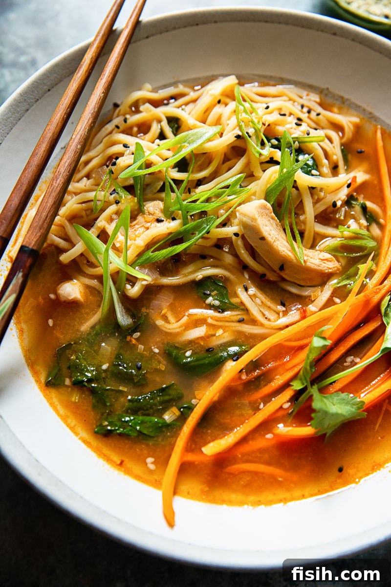 Authentic Thai Noodle Soup Made Easy 5 Close-up of a bowl of Thai Chicken Noodle Soup, showing noodles, chicken, fresh carrots, and green onions.