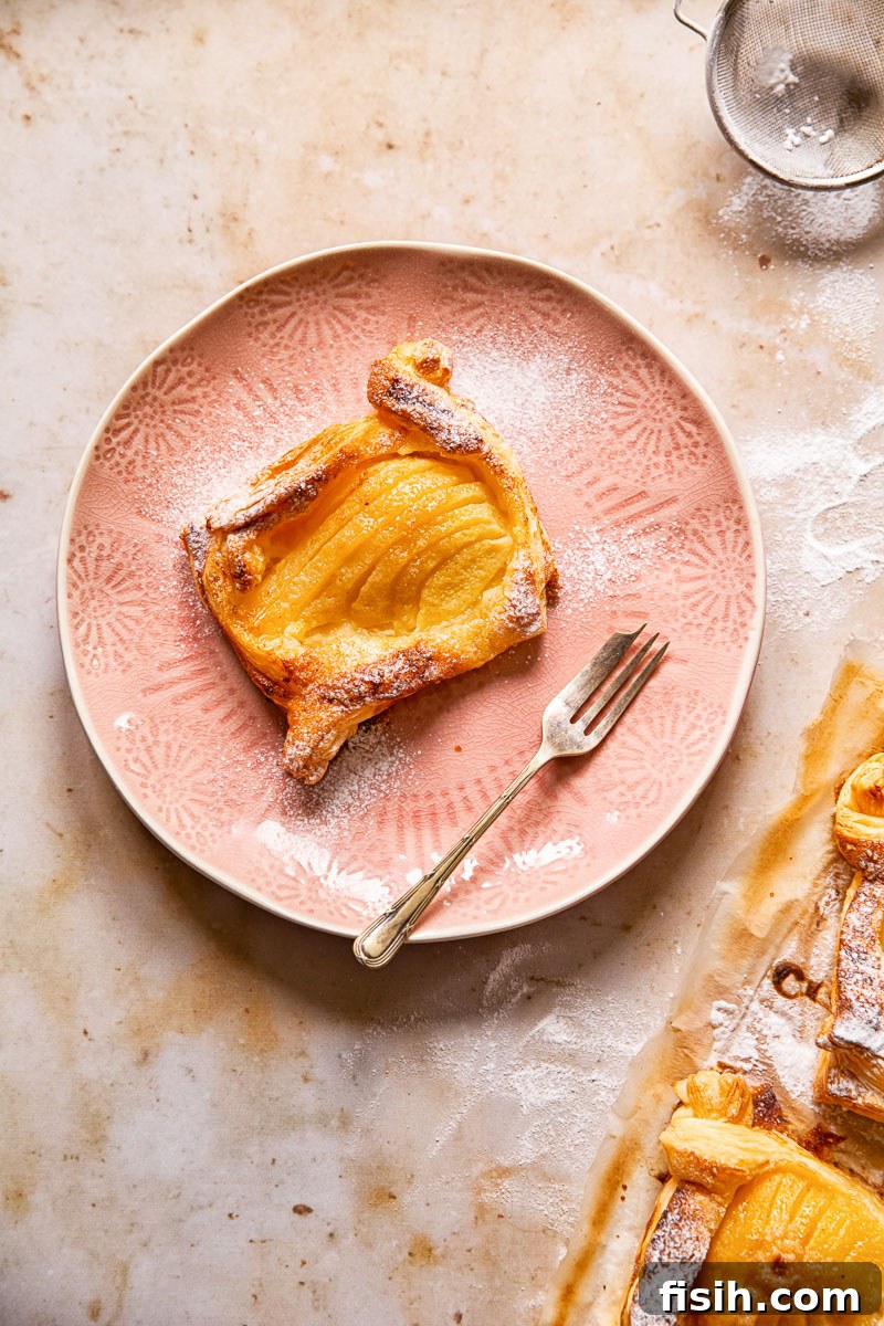 a pear tart on a pink plate with dessert fork and icing sugar