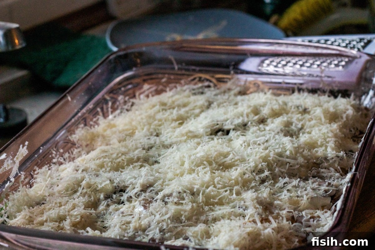 The layered potato dish, now topped with a generous sprinkle of grated sharp cheese, ready for baking.