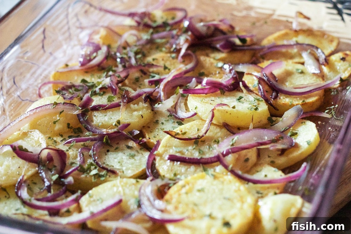 A top-down view of the first layer of golden-brown potato slices arranged neatly at the bottom of a clear baking dish, forming the foundation of the dish.