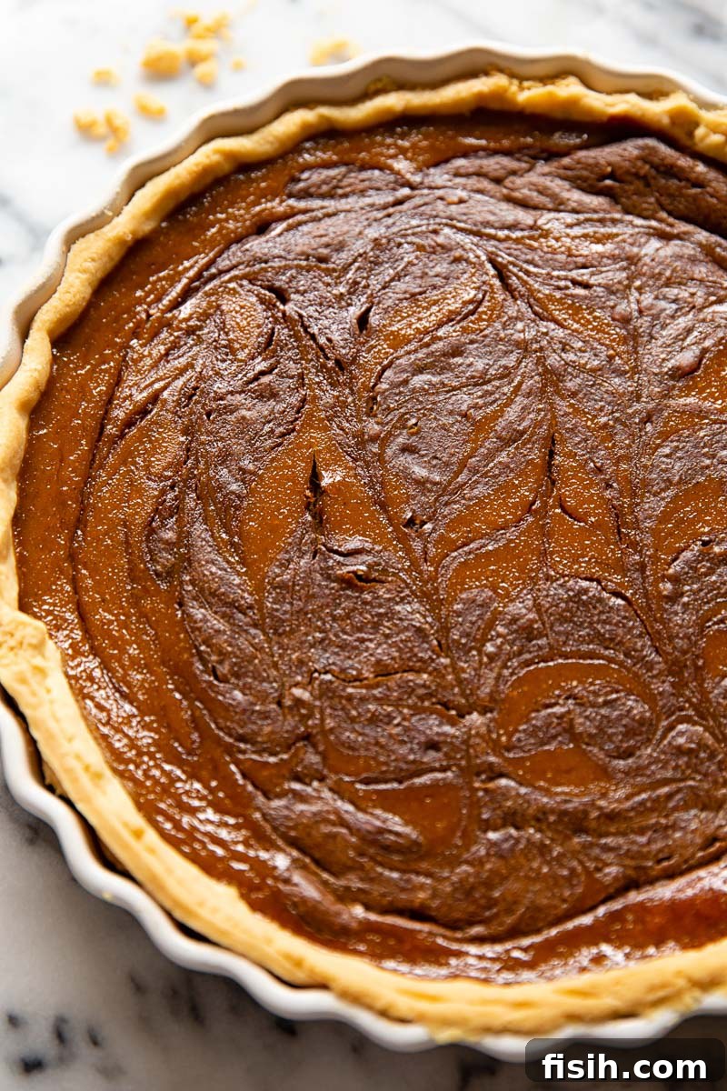 A whole pumpkin pie, beautifully adorned with a chocolate swirl pattern across its surface, waiting to be served.