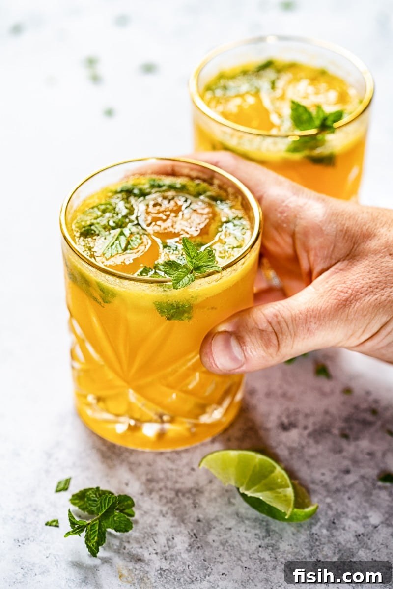 Refreshing Mango Mojito in a glass with a straw, garnished with mint and lime.