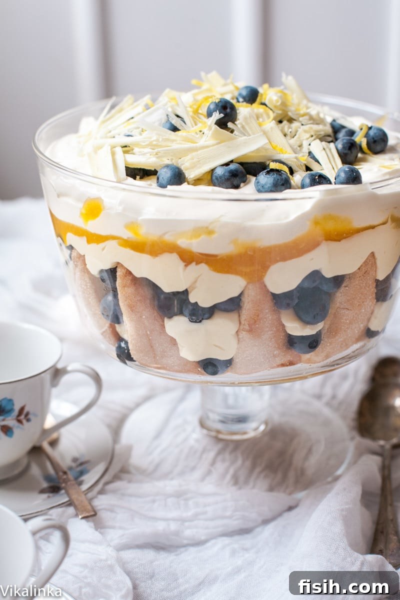 A vibrant Lemon Blueberry Trifle displayed on a white cloth-covered table, accompanied by a charming white and blue teacup, inviting a moment of sweet indulgence.