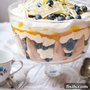 A vibrant Lemon Blueberry Trifle displayed on a white cloth-covered table, accompanied by a charming white and blue teacup, inviting a moment of sweet indulgence.