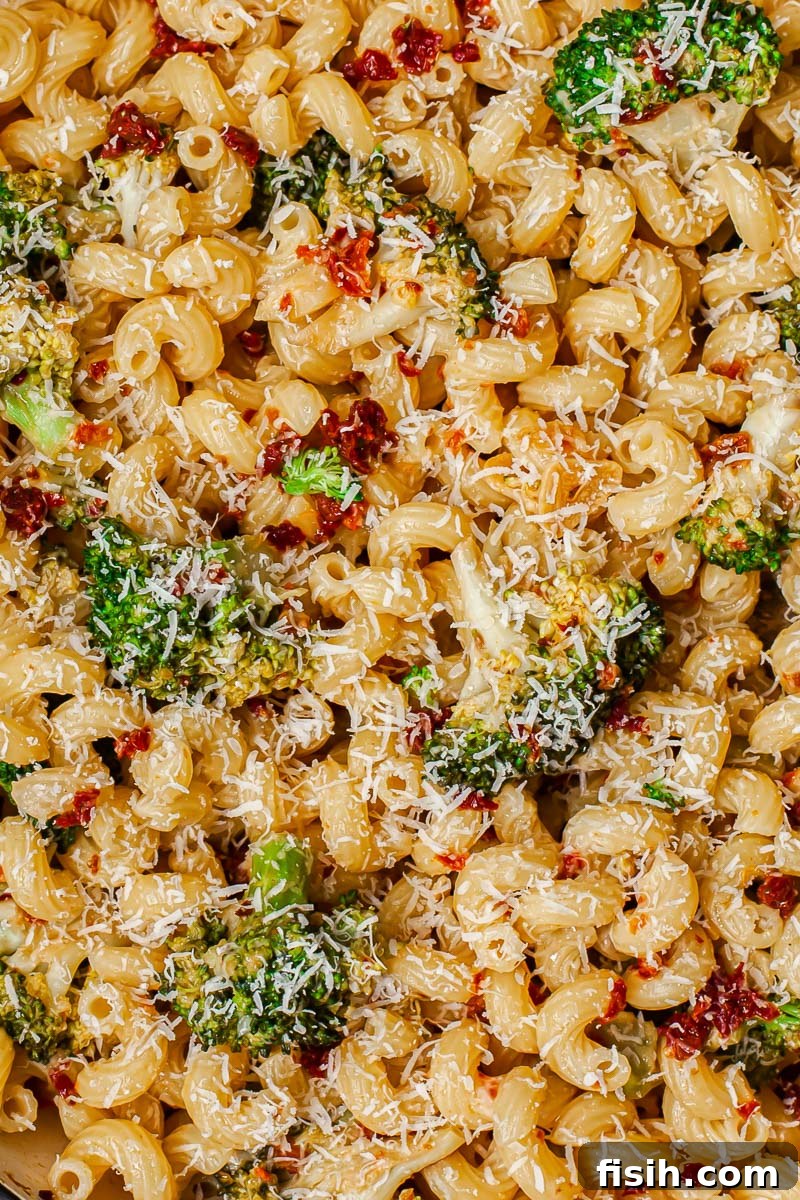 Sun-Kissed Broccoli & Parmesan Pasta 4 A top-down view of a serving of broccoli and sun-dried tomato pasta, generously sprinkled with freshly grated Parmesan cheese, glistening with olive oil.