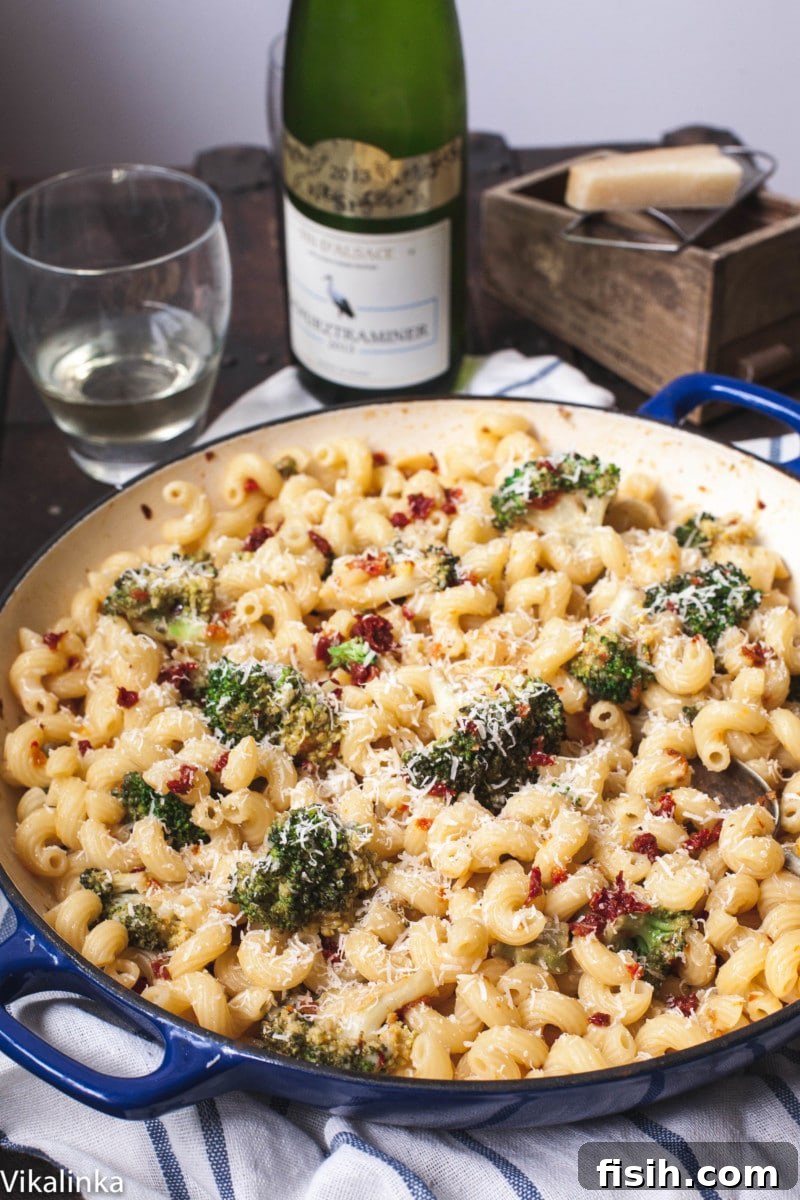 Sun-Kissed Broccoli & Parmesan Pasta 5 A vibrant pasta dish with broccoli and sun-dried tomatoes in a blue pan, accompanied by a bottle of wine, elegant glasses, and a block of Parmesan cheese, creating an inviting dinner scene.