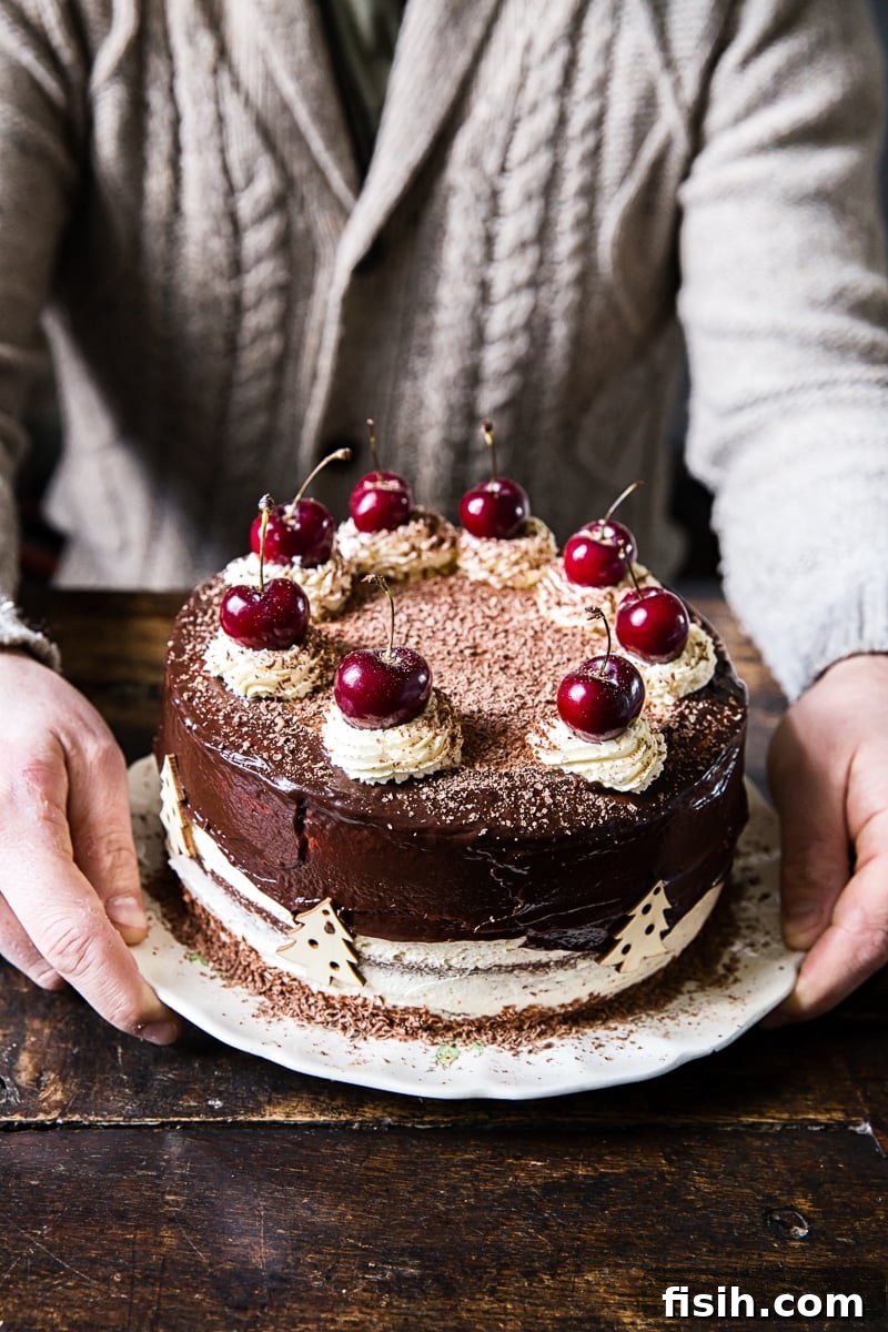 A man proudly holds a beautifully decorated Black Forest Cake, showcasing its luscious layers and rich chocolate ganache drizzle.