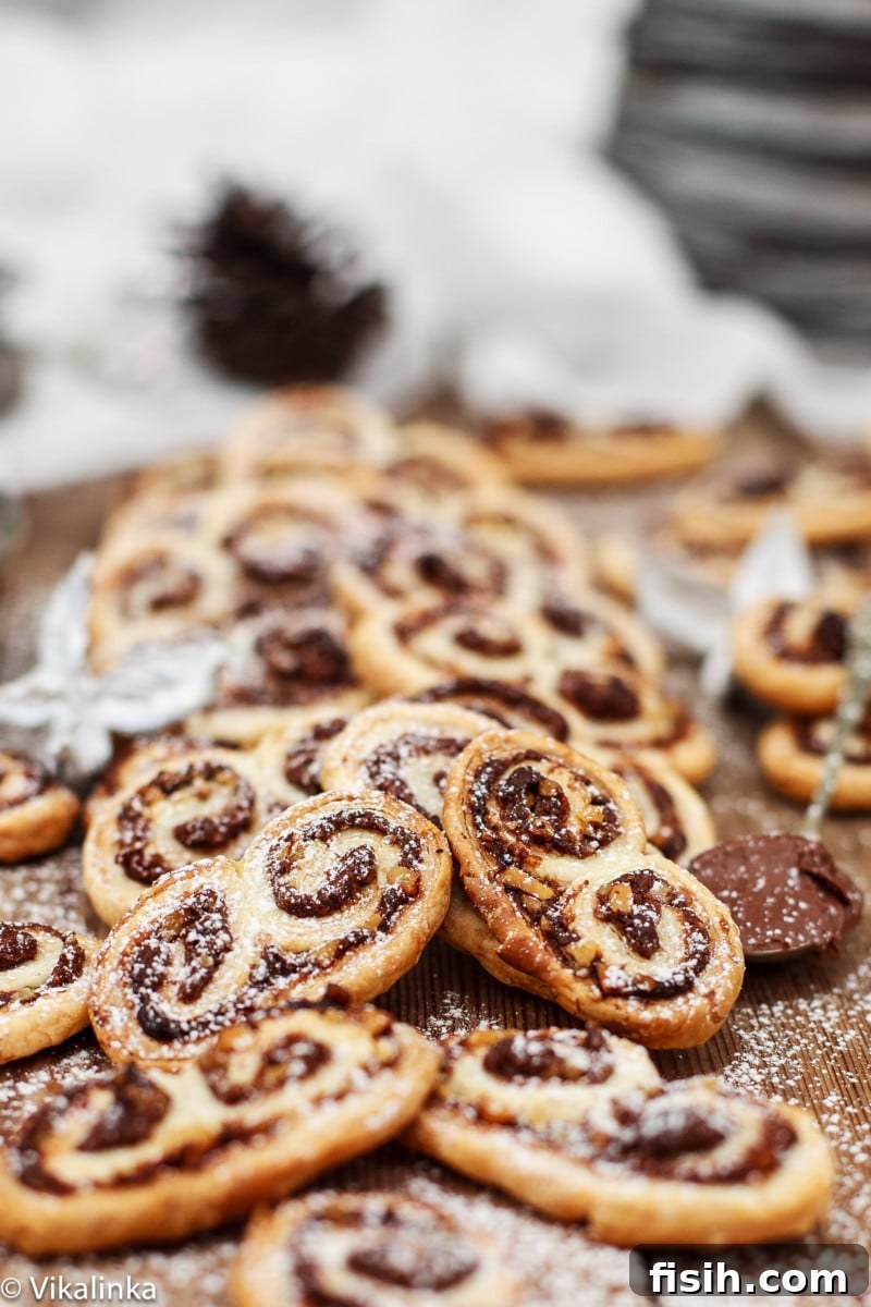 Nutella Swirled Hazelnut Palmiers 2 Side shot of golden-brown Nutella Hazelnut Palmiers, flaky and inviting, arranged on a rustic wooden cutting board, with a hint of festive decor in the background.