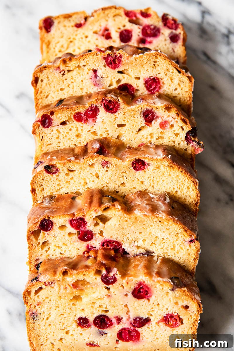 Close-up of freshly baked cranberry orange bread with an orange glaze, showing multiple slices.