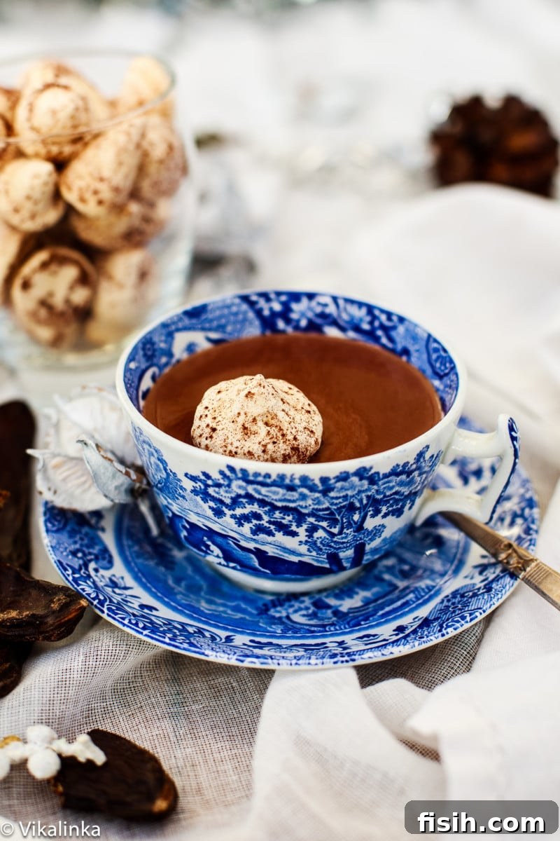A side shot of a cup of thick Italian Hot Chocolate, topped with a delicate white meringue kiss and a sprinkle of cocoa.