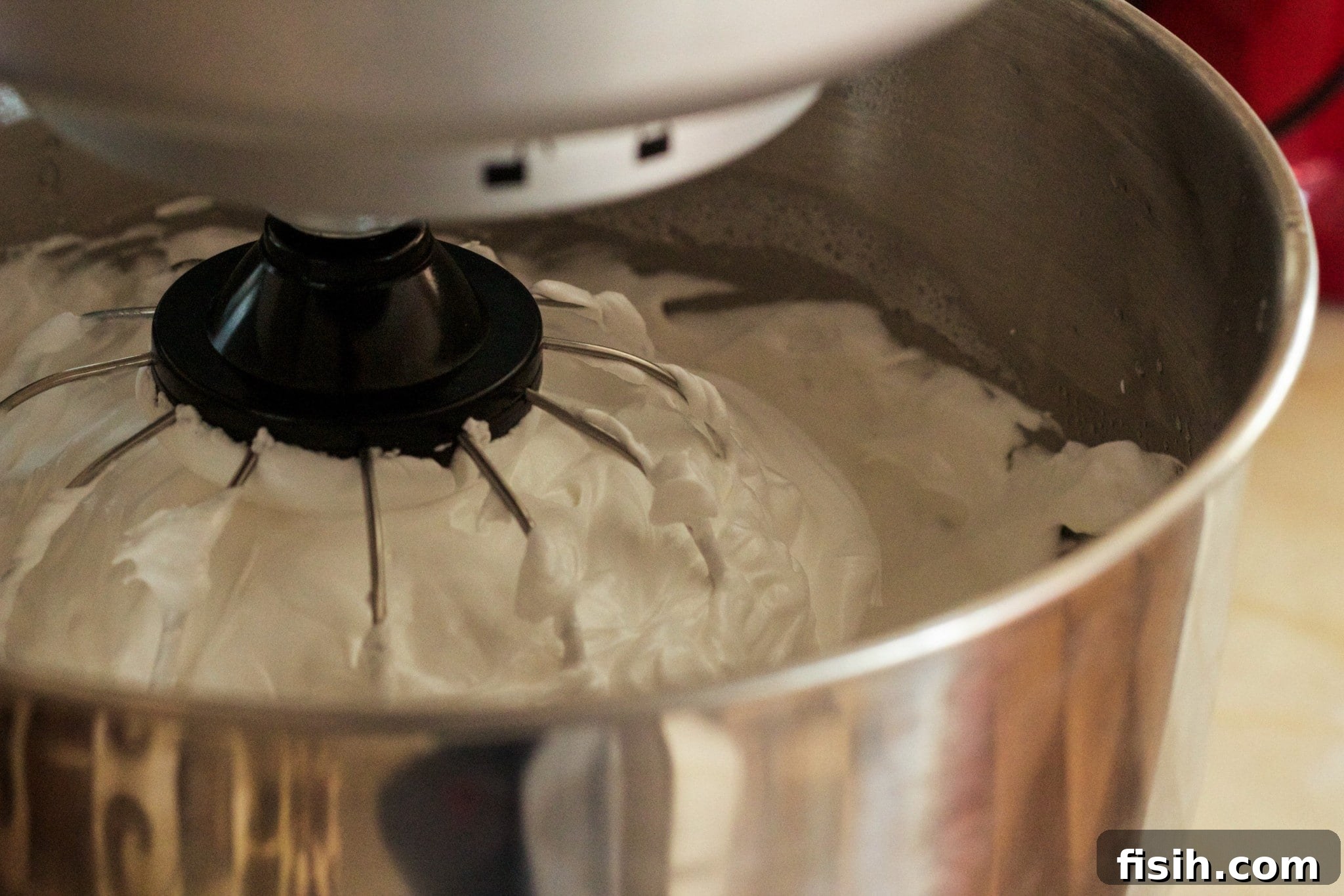 Close-up of fluffy white meringue being mixed in a large bowl, showcasing its light and airy texture as it becomes stiff.