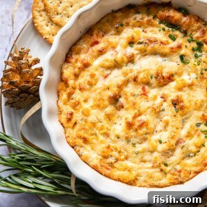 baked crab dip in white round dish with crackers and rosemary around the dish
