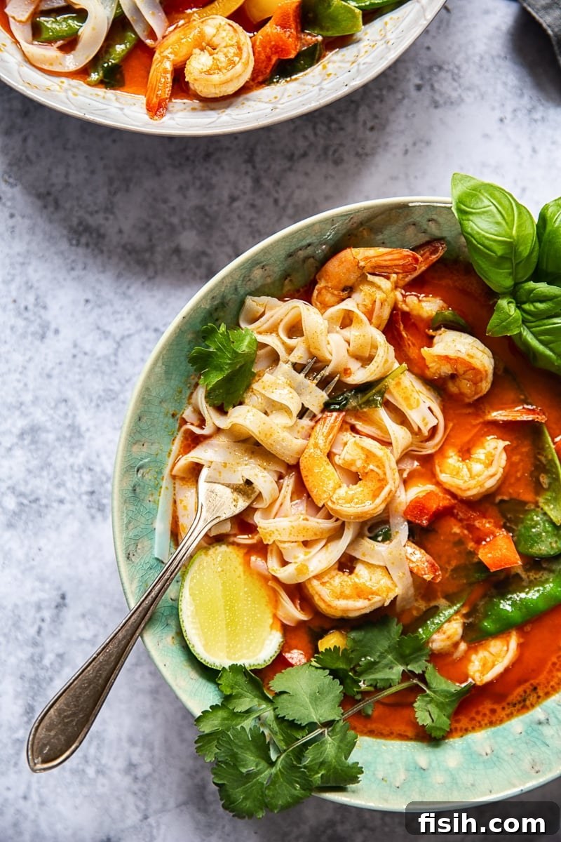 A top-down view of a blue bowl filled with Thai Red Curry, showcasing shrimp, rice noodles, and a vibrant red sauce, garnished with fresh herbs.