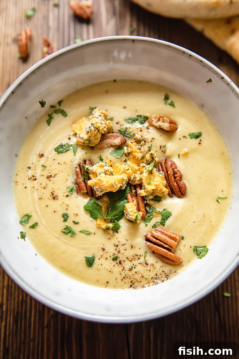 Silky smooth cauliflower cheese soup topped with crumbled Stilton, toasted pecans, and fresh parsley, presented in a rustic bowl.