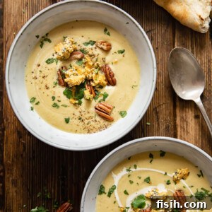 Two bowls of curried cauliflower cheese soup with garnishes on a wooden surface.