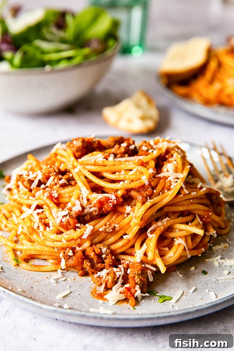 Classic Spaghetti Bolognese 2 Classic spaghetti bolognese served on a grey plate with a fresh green salad in the background, ready for a comforting meal.