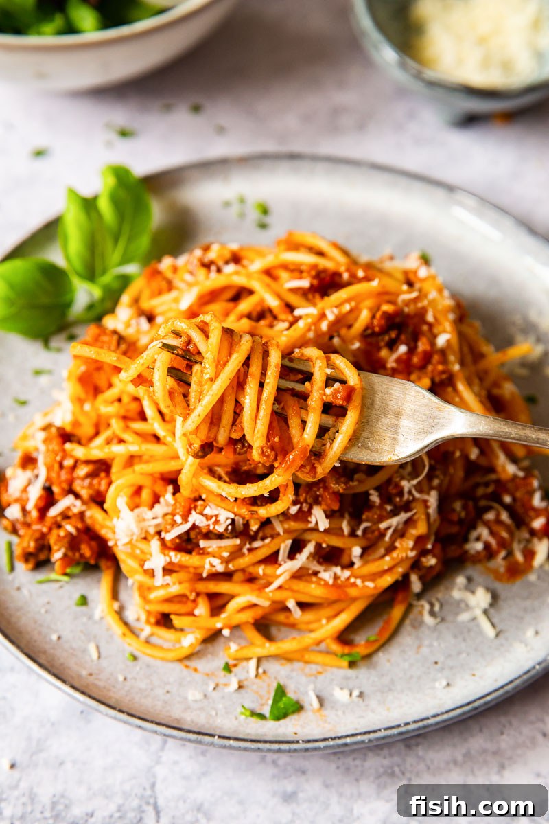 Classic Spaghetti Bolognese 5 A fork coils a perfect bite of spaghetti, lifted from a plate piled high with rich, meaty Bolognese sauce.