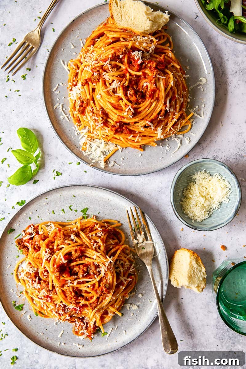 Classic Spaghetti Bolognese 6 An overhead view of two grey plates, each holding a generous serving of spaghetti topped with rich, red meat sauce.