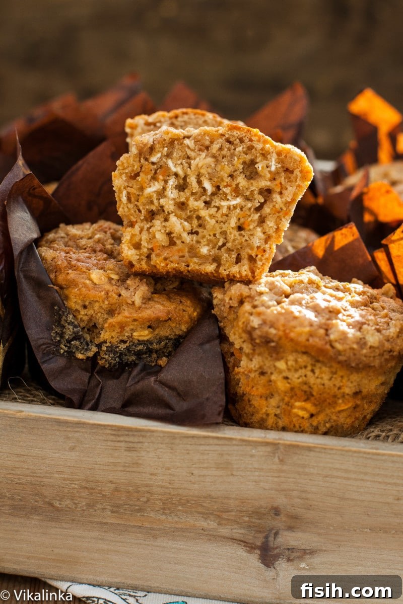 A close-up shot of carrot oatmeal muffins nestled in a bread box, with one muffin sliced to showcase its moist and tender crumb.