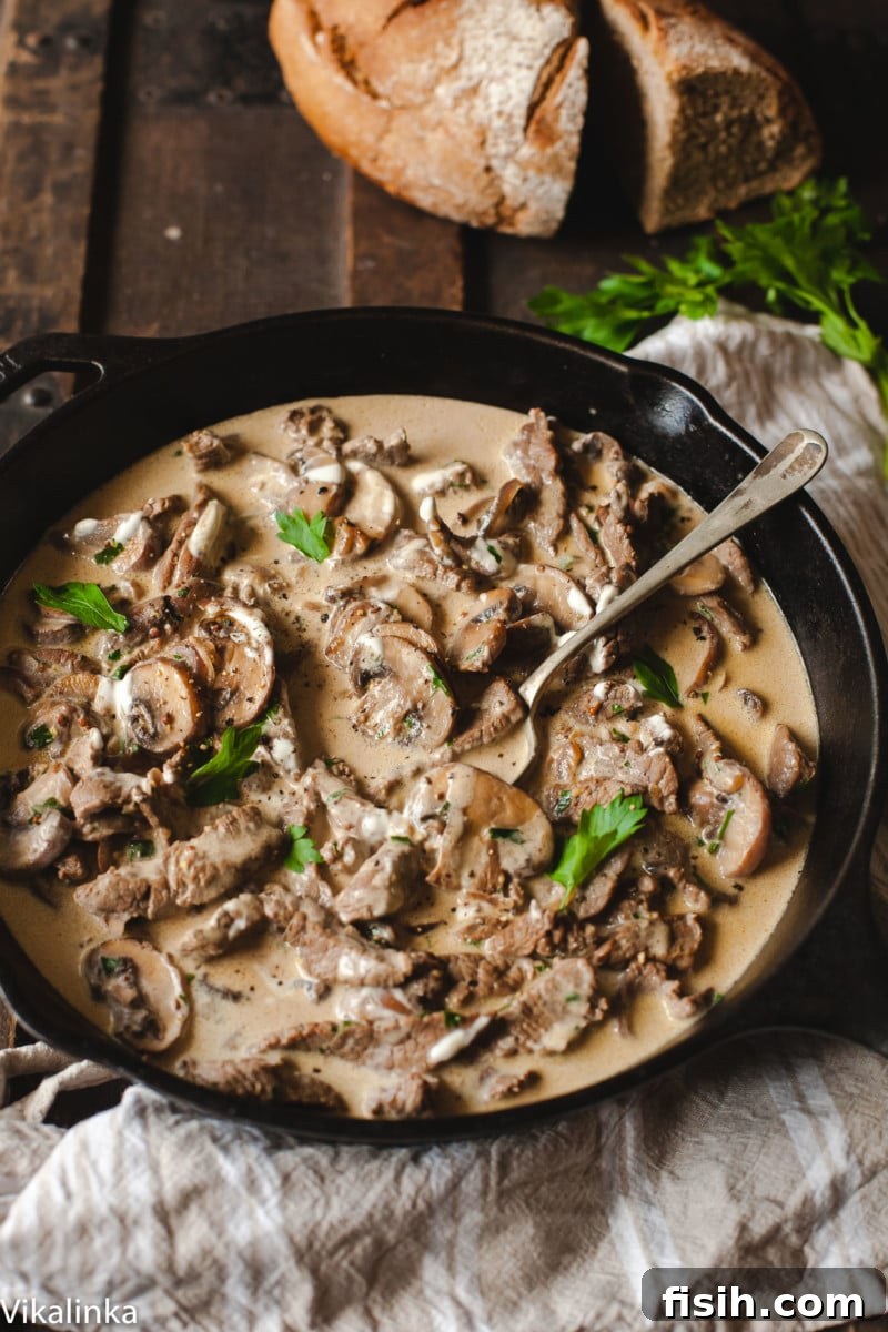 beef stroganoff in black pan on wooden table, loaf of bread in the background