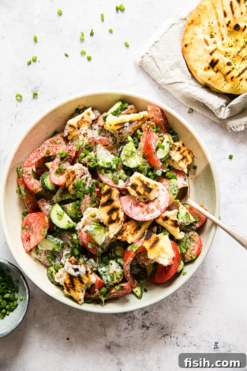 Tangy & Crisp Fattoush Salad 3 Overhead shot of Fattoush salad in a cream-colored bowl, accompanied by a spoon, grilled flatbread, and a small bowl of sliced green onions, ready for serving.