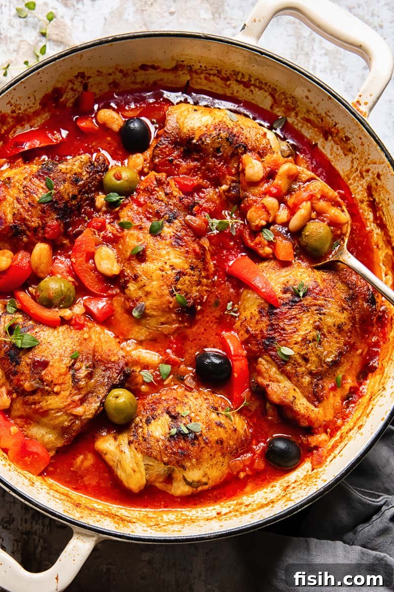 Spanish Chicken with red peppers, olives and white beans in a vibrant tomato sauce, served in a cast iron pan.