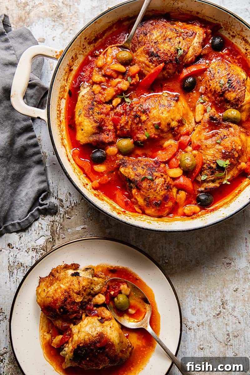 Plated Spanish chicken thighs with red peppers and olives in a tomato sauce, accompanied by white beans and a spoon, ready to be enjoyed.