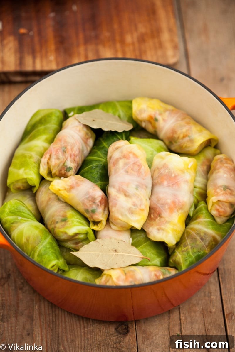 Freshly prepared Cabbage Rolls (Golubtsi) arranged in a cast-iron casserole dish, topped with bay leaves and ready for the rich tomato and sour cream sauce.