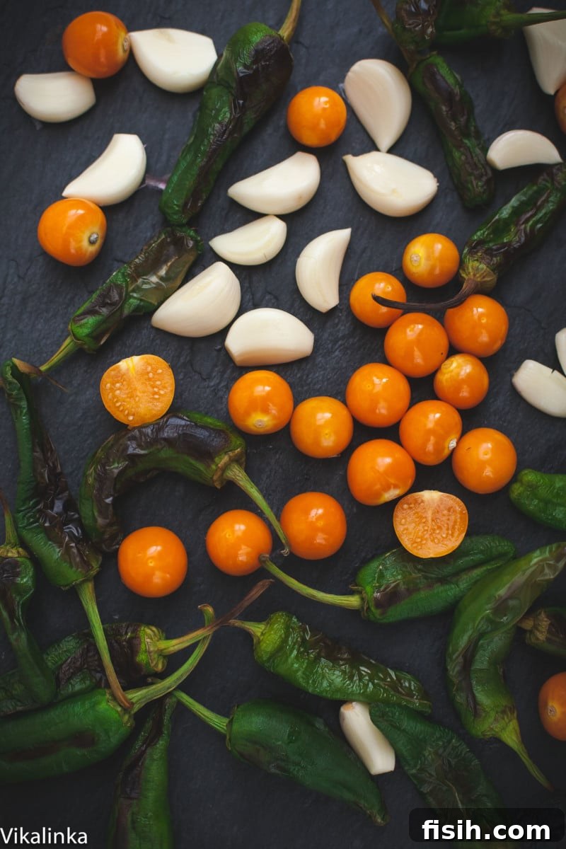 A close-up shot of the fresh ingredients for chile verde, including physalis, vibrant padron peppers, green chillies, and garlic cloves, ready for preparation.