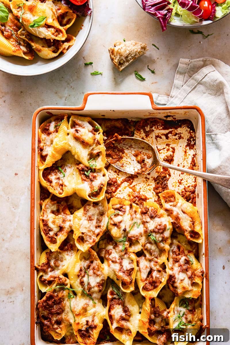 Quick Pesto Beef and Tomato Shells 5 Rectangular baking pan filled with baked pasta shells, alongside a bowl of salad and a serving bowl of pasta