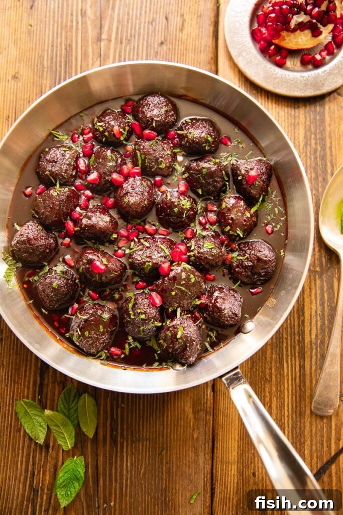 Top down view of glistening sweet and sour meatballs served on a wooden table, garnished with fresh herbs and pomegranate seeds.