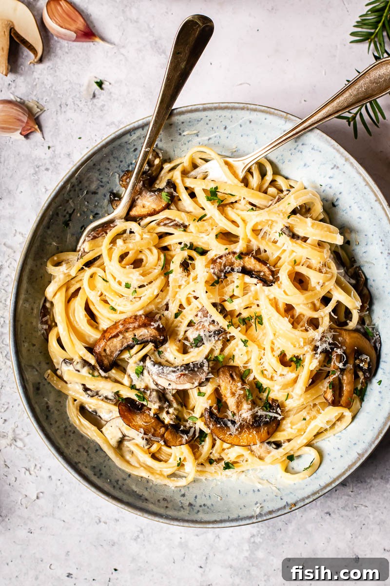 Rich Truffle Cream Tagliatelle with Crispy Bacon and Forest Mushrooms 4 Top down view of a bowl with creamy pasta, bacon, and mushrooms, garnished with fresh herbs.