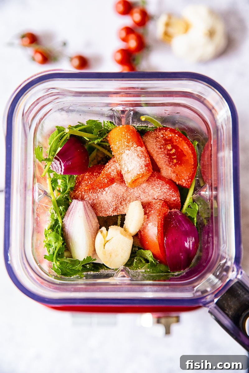 Fresh salsa ingredients, including quartered tomatoes, onions, cilantro, and chilies, placed inside a blender
