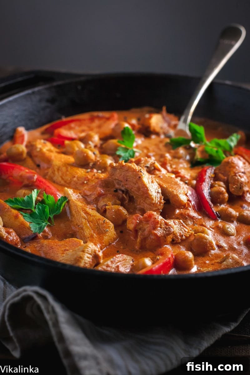 Side view of tender chicken pieces in a vibrant red paprika sauce, complemented by bell peppers, simmering in a cast iron skillet.