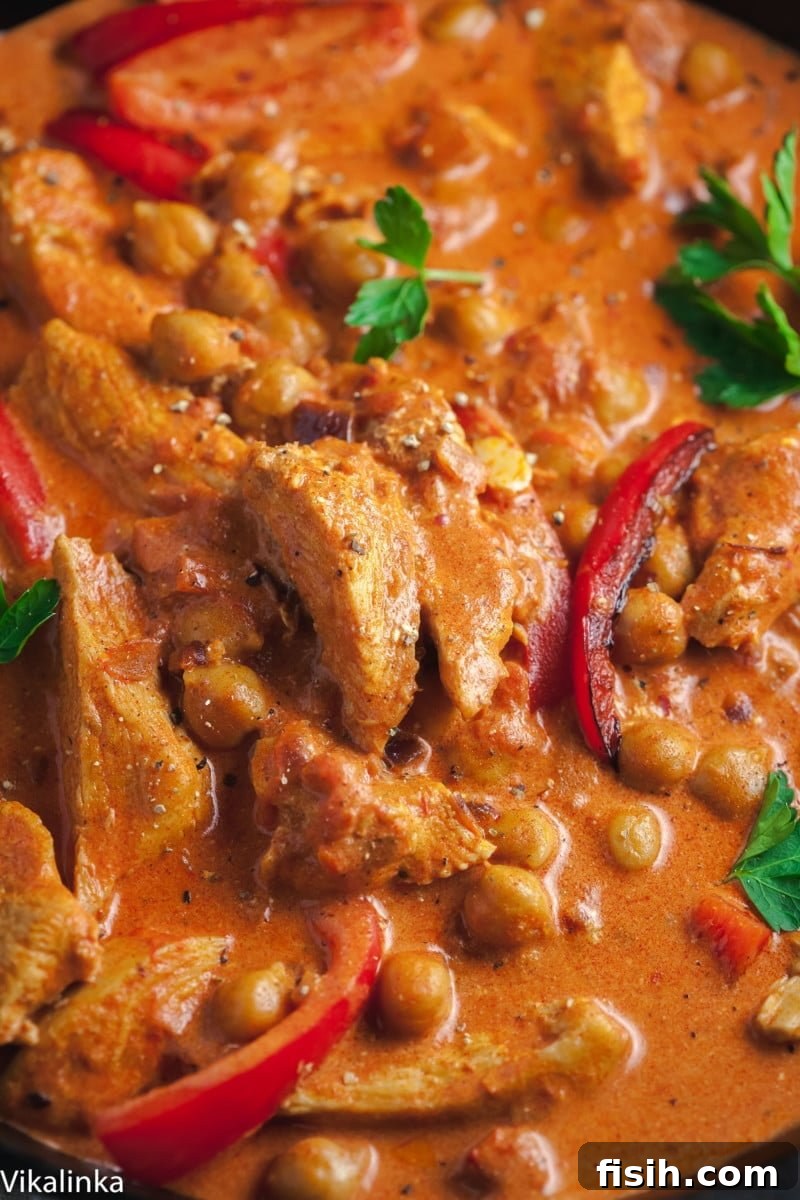 A close-up view of a serving of chicken paprikash, rich with chickpeas and vibrant red peppers, topped with fresh parsley.