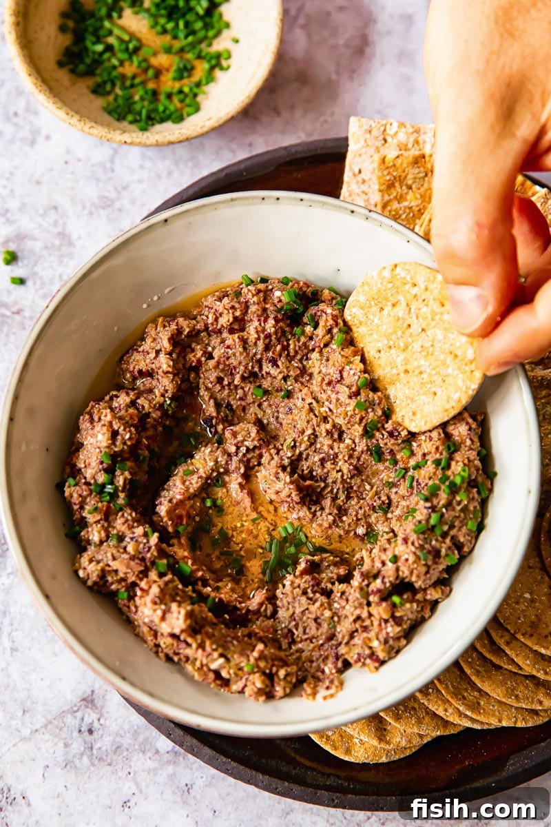 Creamy Feta Olive Tapenade 3 a cracker being dipped into a bowl of homemade olive tapenade, highlighting its inviting texture
