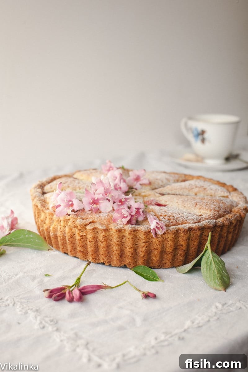 Bakewell tart decorated with pink flowers on a table covered with white tablecloth