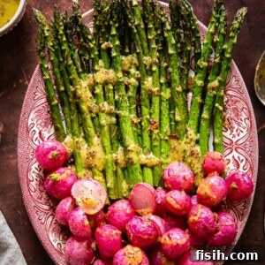 Top-down view of beautifully roasted asparagus and radishes drizzled with a golden mustard vinaigrette, presented on a rustic platter.
